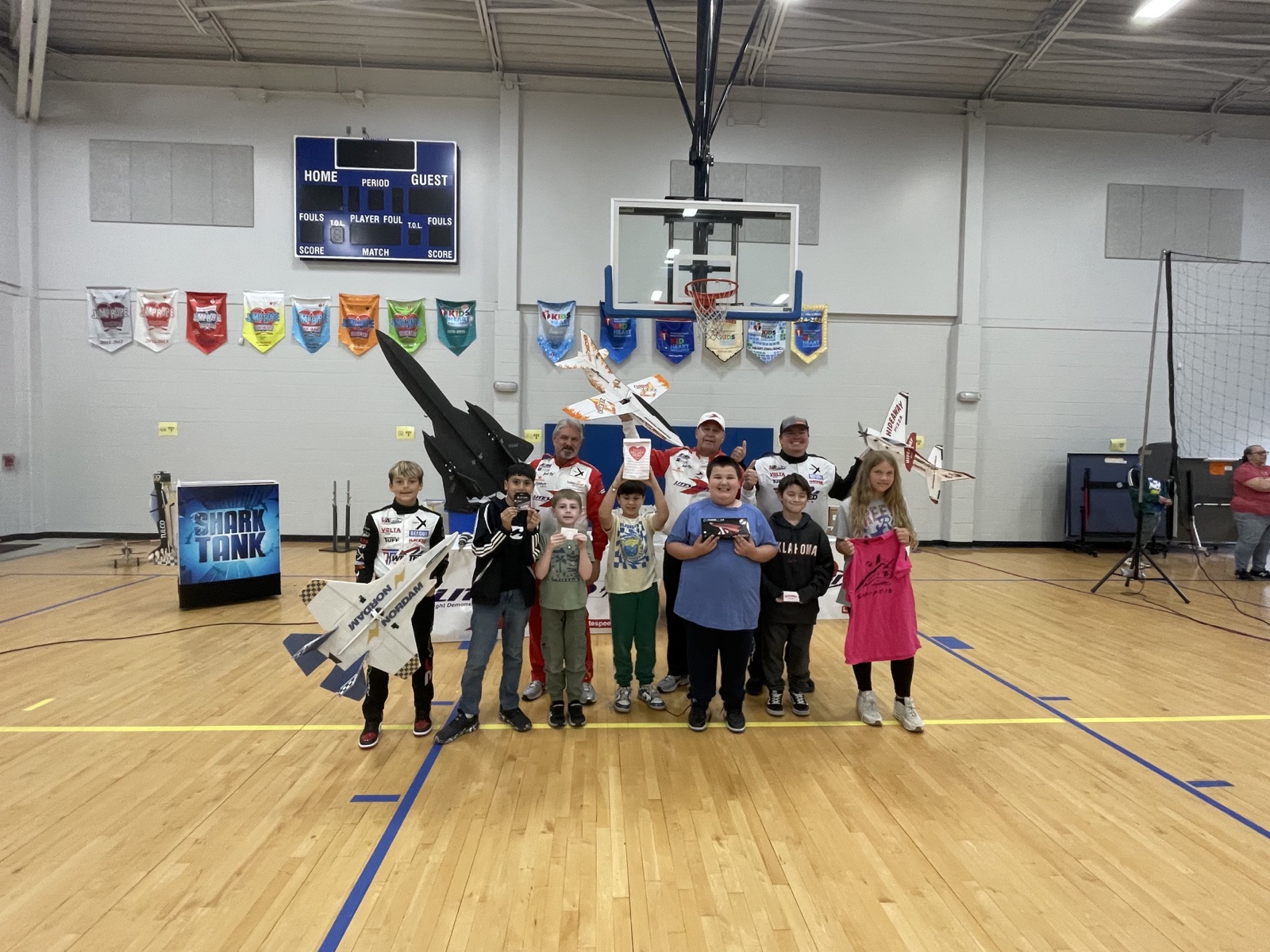 Litespeed Airshow presenters and students posing with radio-controlled aircraft in a school gym
