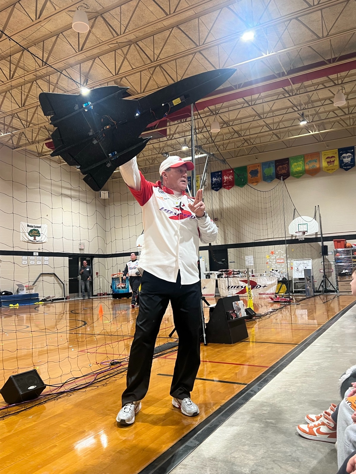 Litespeed presenter holding a black radio-controlled jet above his head during a school gym demonstration