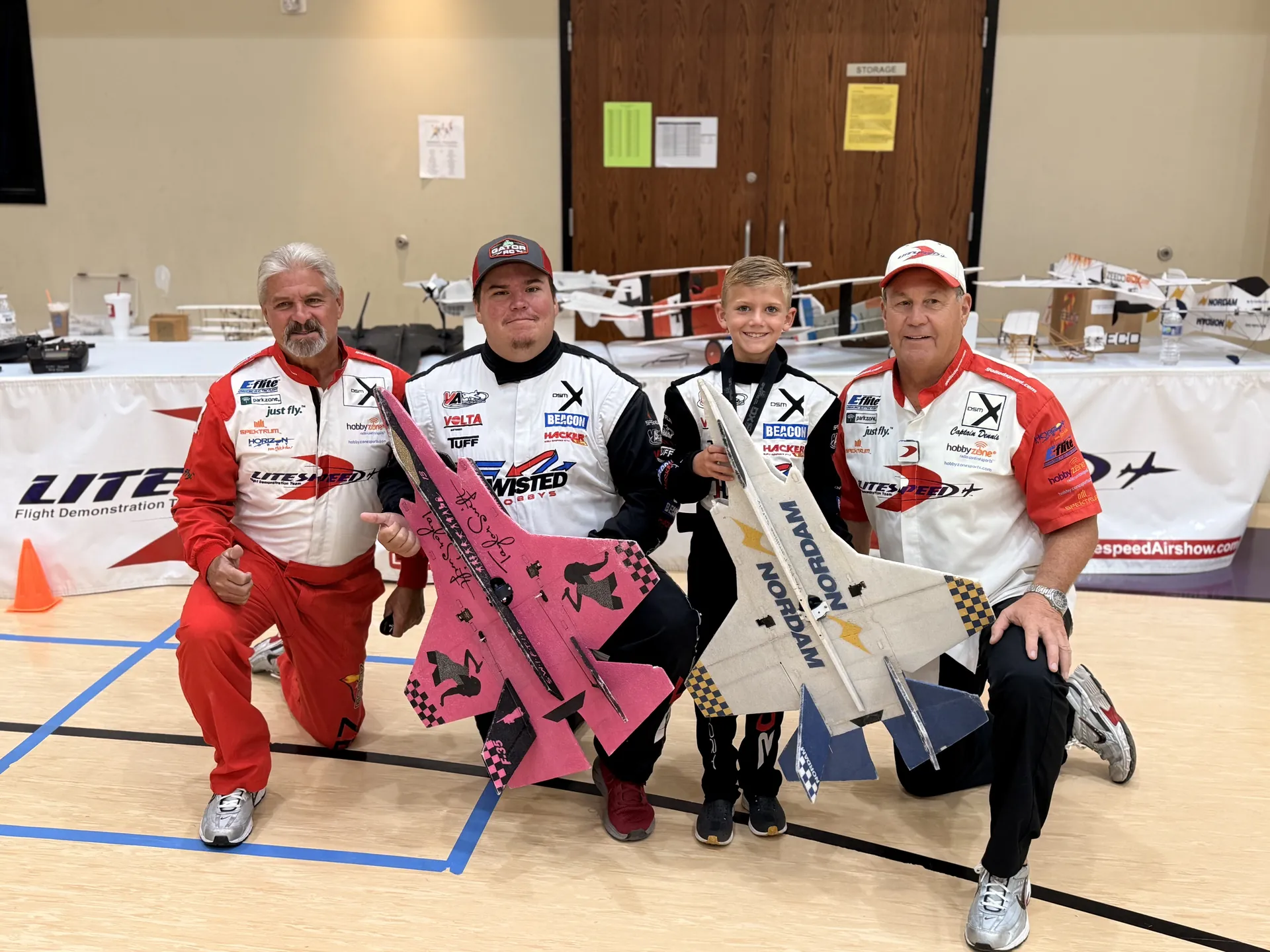 Litespeed Airshow pilots and a young student pilot posing with radio-controlled aircraft in a school gym