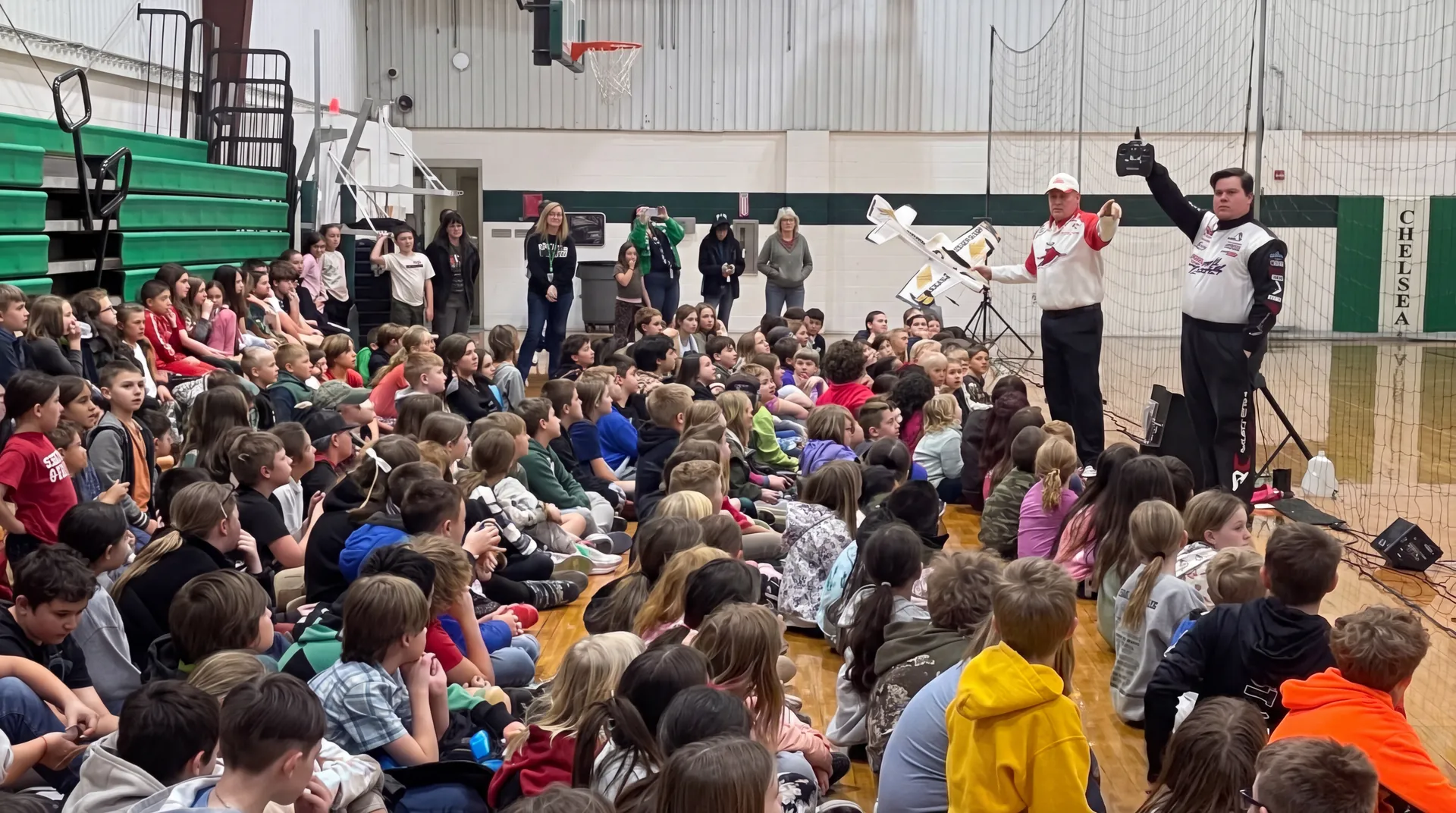 Elementary students watching Litespeed Airshow presenters demonstrate a radio-controlled aircraft in a school gym